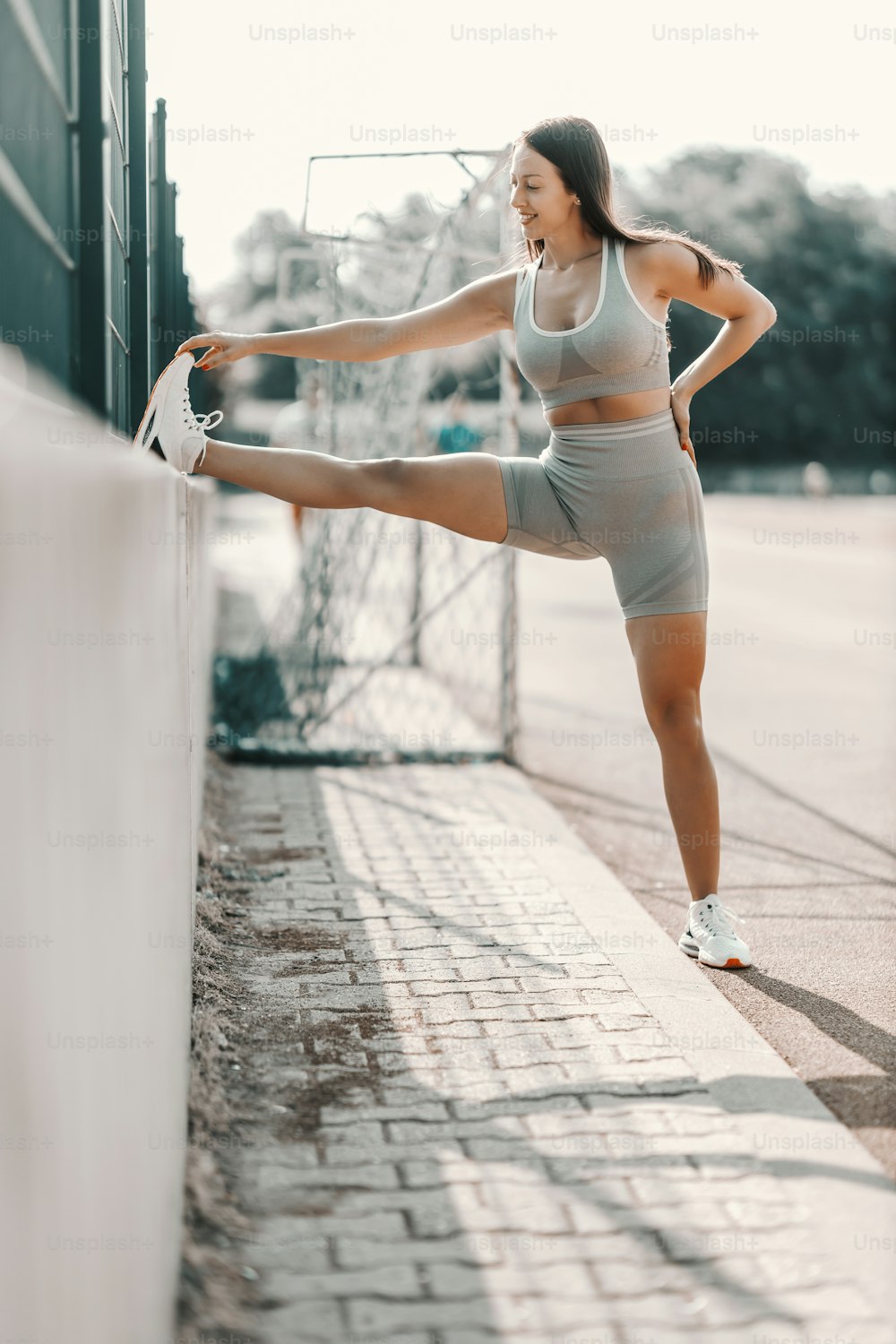 Stretching leg muscles in training. A woman in tight fitness clothes stretches her leg muscles during a workout. She has raised her foot on the concrete fence and is preparing for a street workout