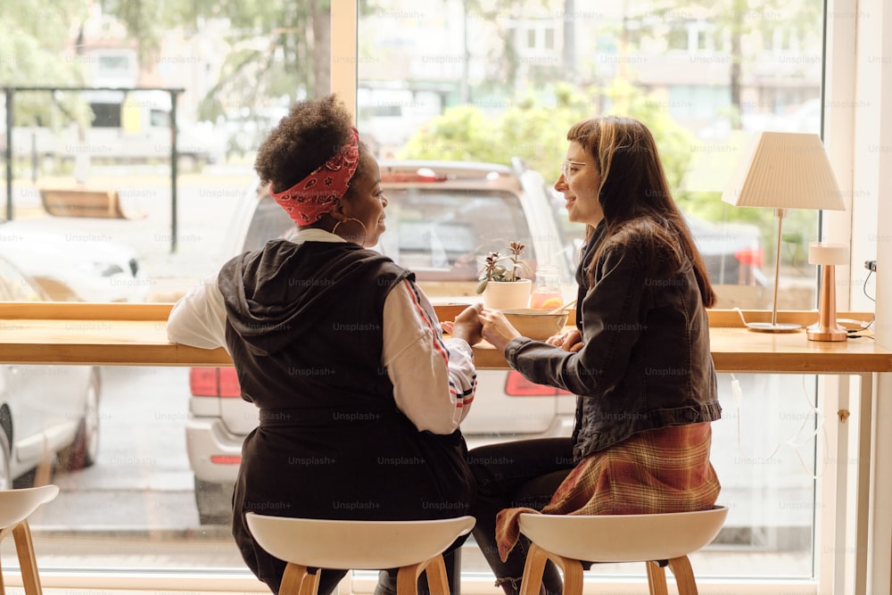 Feliz jovem casal lésbico segurando por h ands enquanto almoçava na frente da janela no café