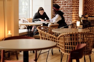 Two affectionate girlfriends choosing lunch in menu while sitting in cafe