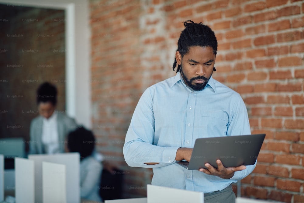 Hombre de negocios negro usando una computadora portátil mientras trabaja en una oficina corporativa.