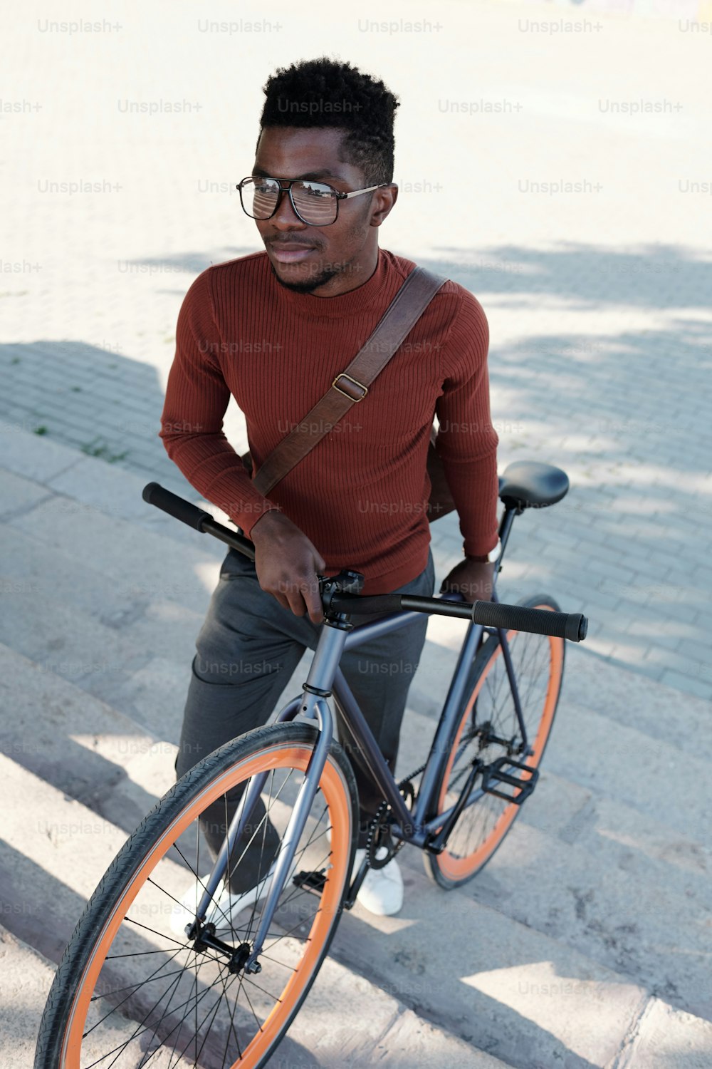 안경과 스마트 캐주얼웨어를 입은 젊은 사업가가 야외에서 위층으로 올라가는 동안 자전거를 밀고 있다