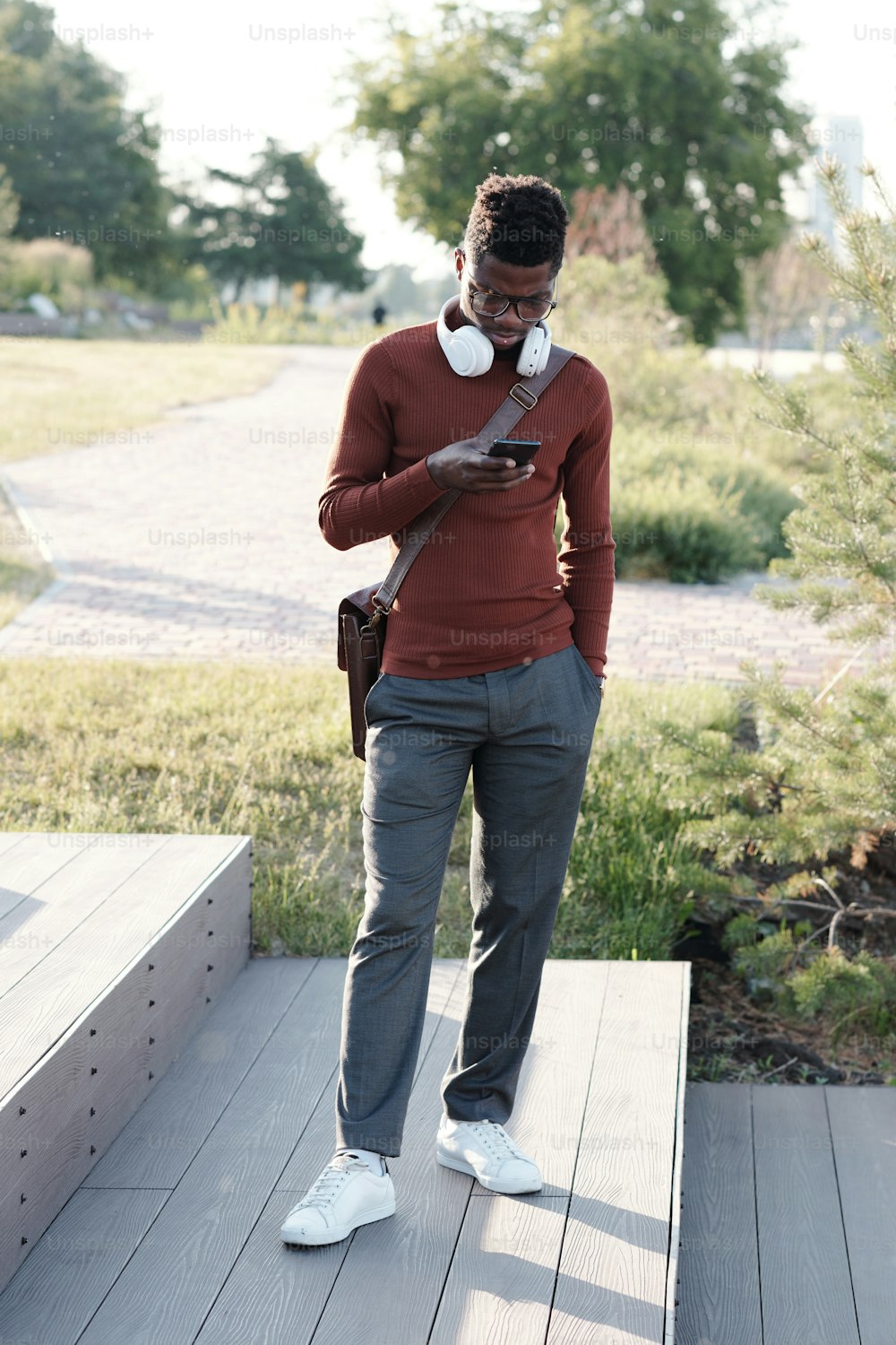 Young African man with headphones on neck scrolling or texting in mobile gadget