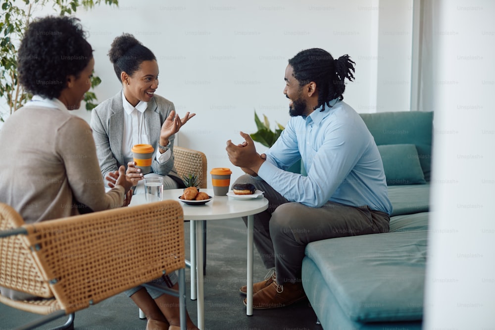 Happy black entrepreneurs enjoying while communicating during coffee break at work.