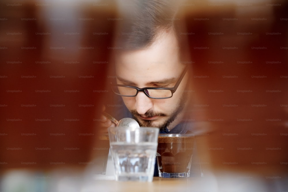 Portrait of man smelling freshly brewed coffee in glass cup, using spoon, examining coffee taste and flavour at coffee cupping test for barosta