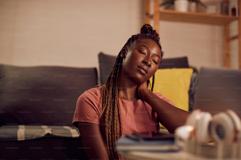Jovem estudante negra cansada relaxando com os olhos fechados depois de usar laptop e aprender à noite em casa.