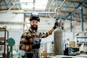 Un ouvrier avec un masque de protection sur la tête s’apprête à effectuer des travaux de soudure dans son atelier. Ouvrier avec une machine à souder.