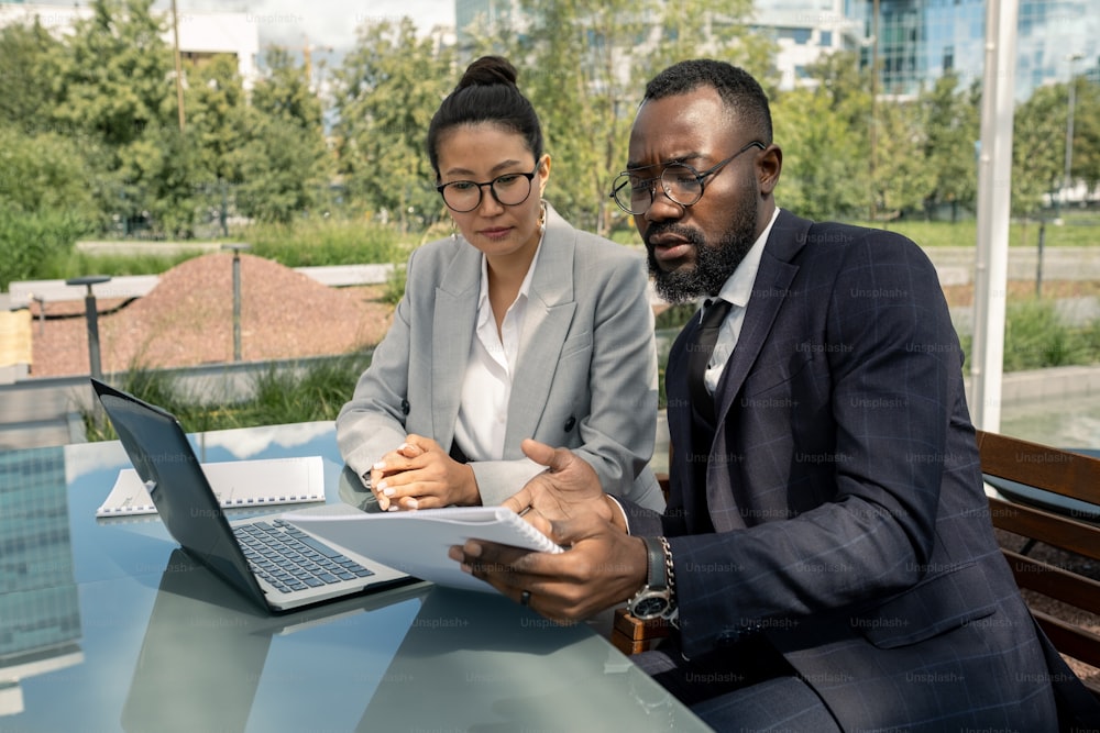 African businessman showing paper to Asian female business partner at outdoor meeting