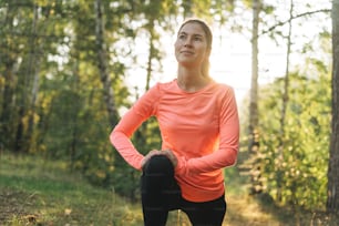 Junge schlanke Frau brünett in Sportkleidung beim Stretching im Wald zur goldenen Stunde Sonnenaufgangszeit. Gesundheit und Wellness, Fitness Lifestyle