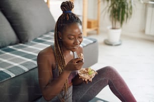Happy African American sportswoman working out at home and eating healthy food.