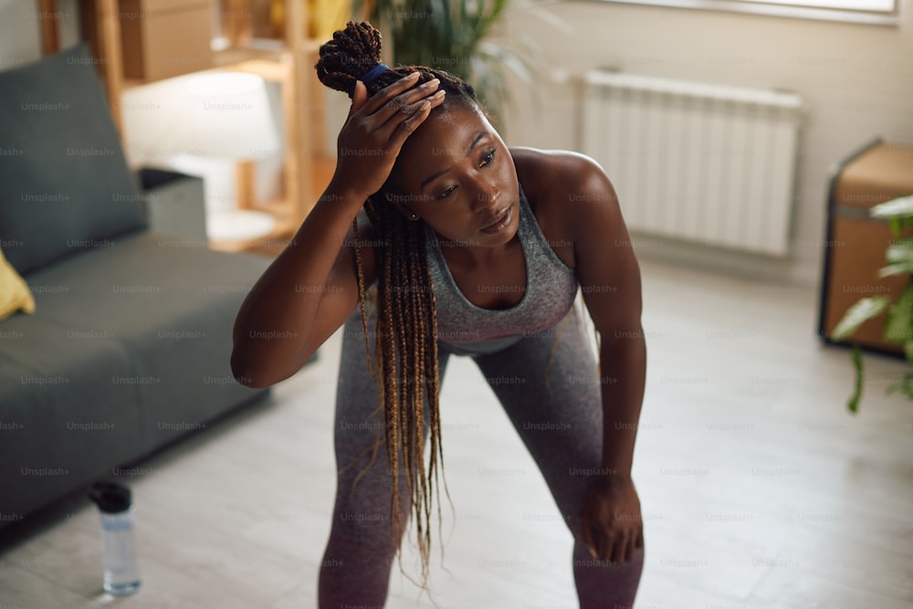Deportista afroamericana cansada que se toma un descanso mientras hace ejercicio en casa.