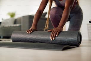 Gros plan d’une sportive noire déroulant son tapis d’exercice tout en se préparant à une séance d’entraînement à domicile.