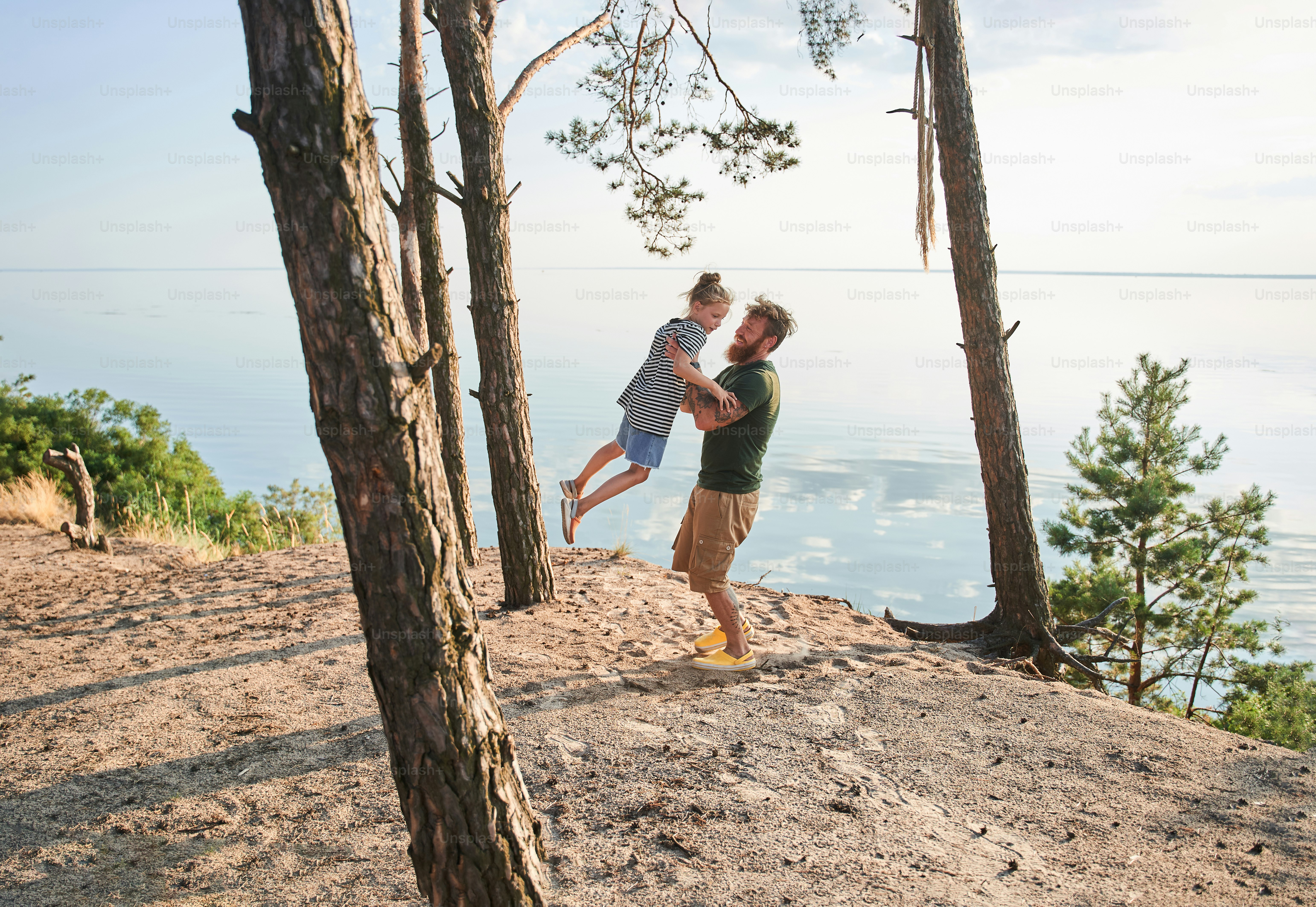 Gemeinsam Spaß haben. Lustiges Mädchen, das laut lacht, während ihr geliebter Vater sie an den Händen hält und in der Luft kreist. Konzept der glücklichen Kindheit