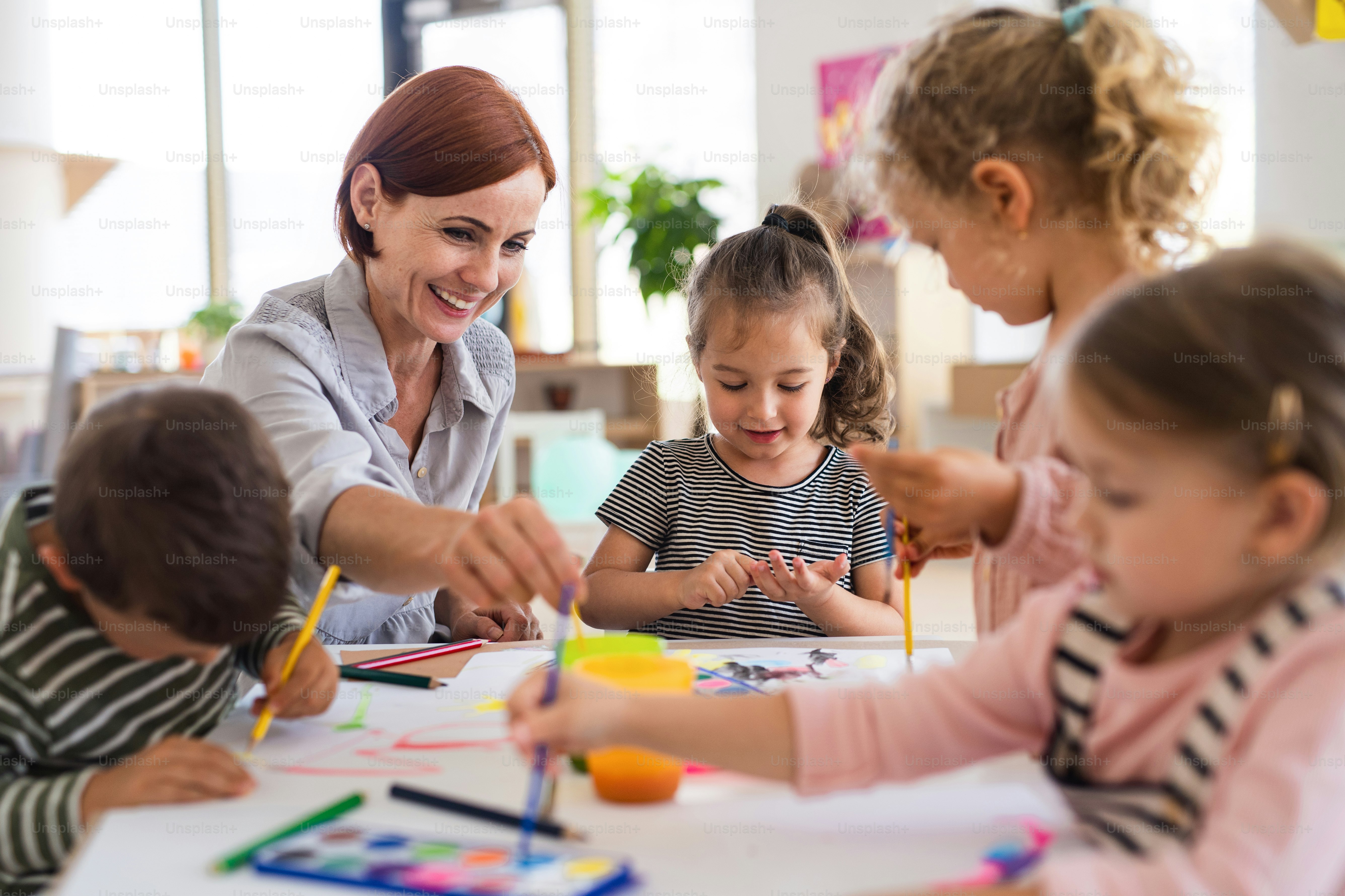 Un grupo de pequeños niños de guardería con maestra en el interior del aula, pintando.