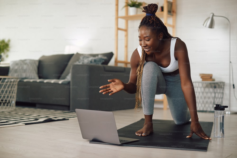 Mujer atlética afroamericana feliz hablando durante una videollamada mientras hace ejercicio en casa.