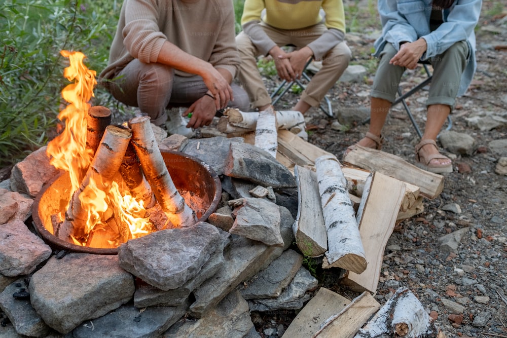 Família repousante de três pessoas sentadas à beira da fogueira enquanto desfruta de viagem em ambiente natural