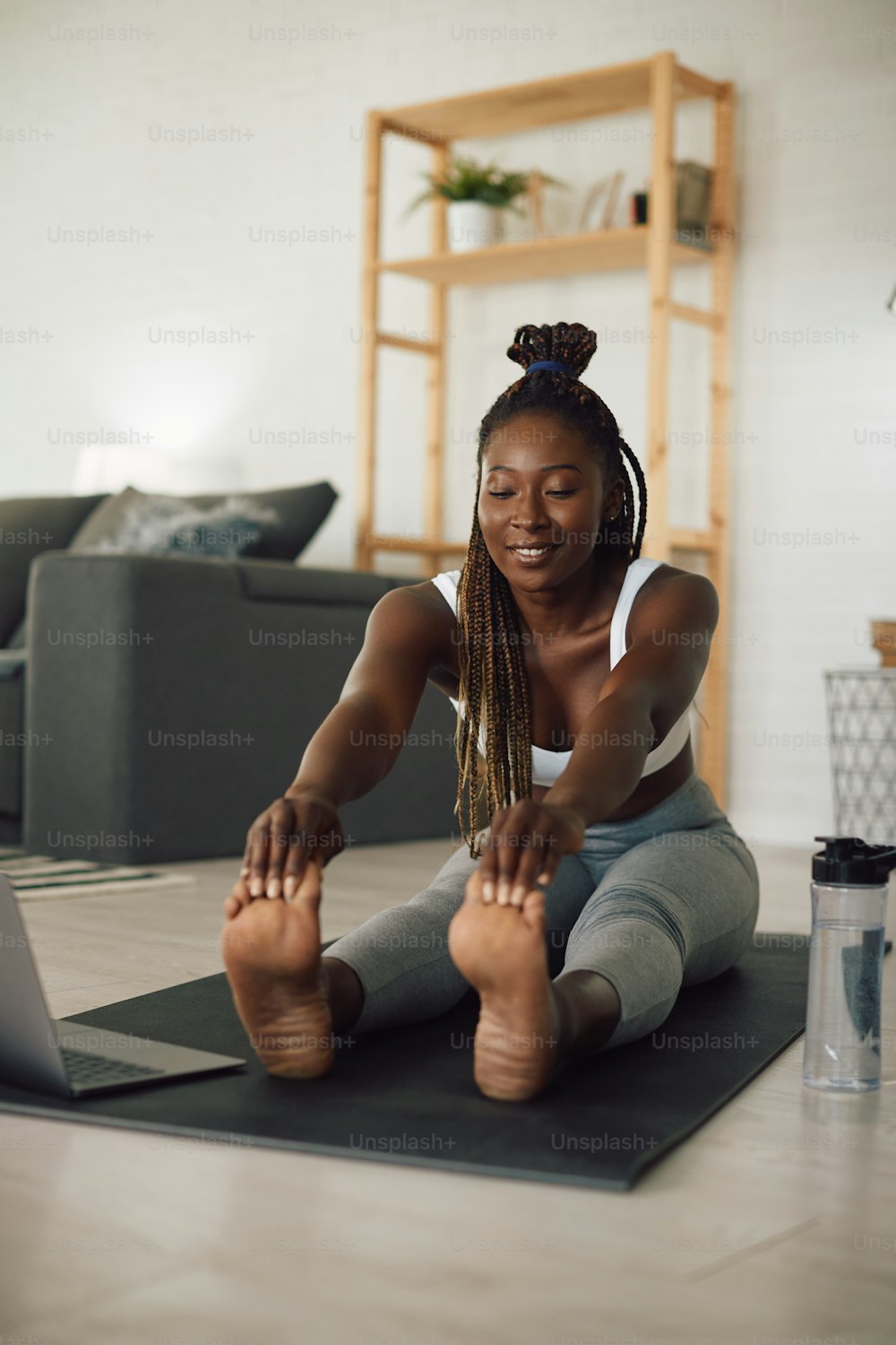Young black female athlete warming up while doing stretching exercises during home workout.