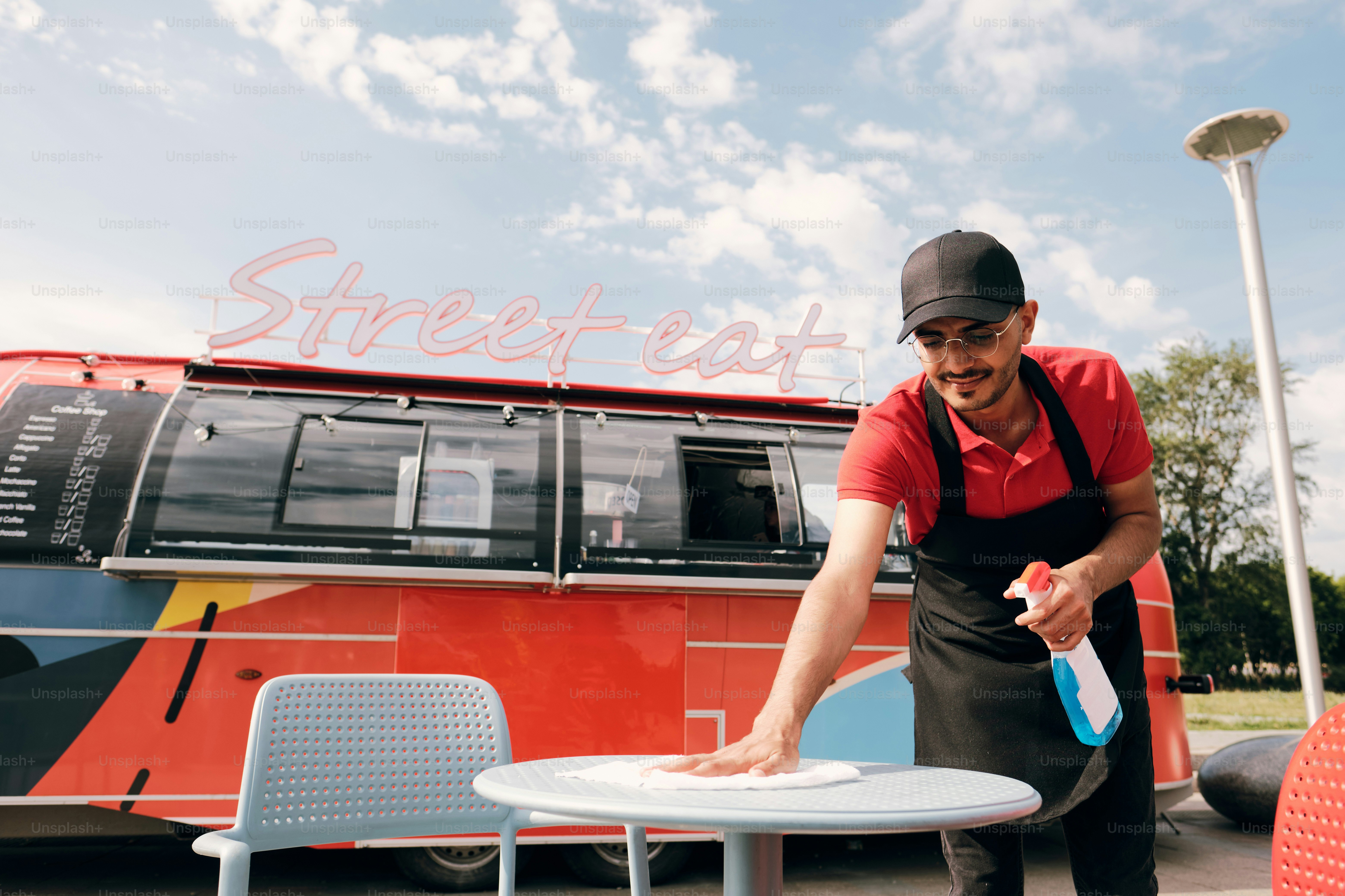 Young man in uniform spraying sanitizer on plastic table while cleaning it in the morning