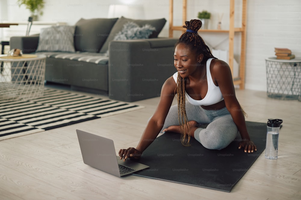 Young African American female athlete using laptop during home workout.