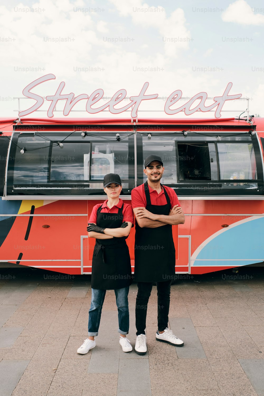 Zwei junge erfolgreiche Arbeiter eines Imbisswagens stehen gegen roten Lieferwagen