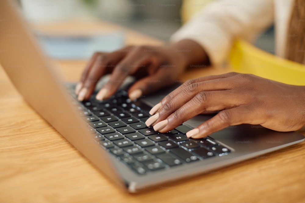 Primer plano de una mujer negra escribiendo un correo electrónico mientras trabaja en una computadora portátil en casa.