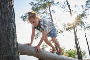 Happy child playing in the forest and climbing on the tree. Cute caucasian girl spending time at the big branch of the tree. Childhood concept