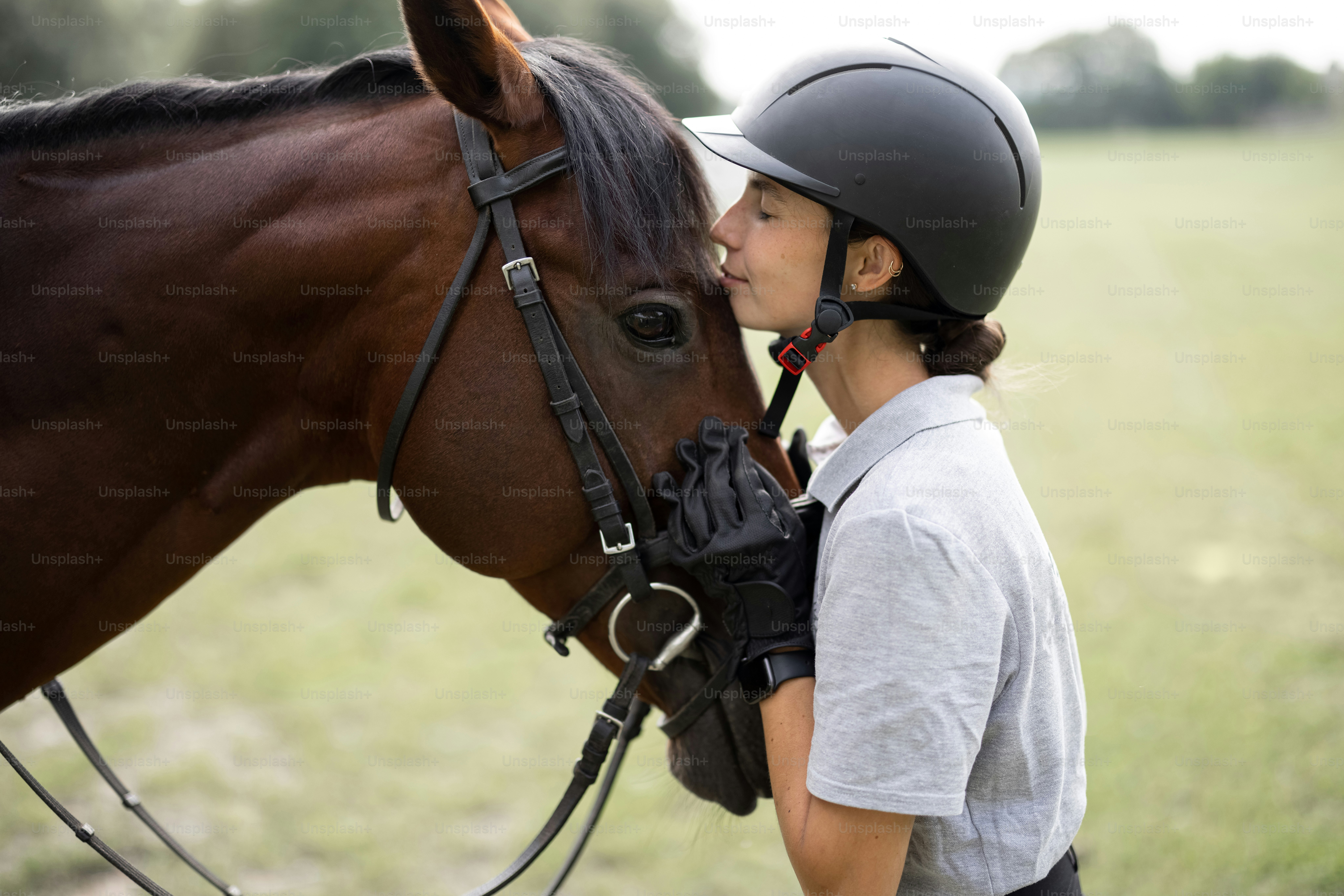 Femme cavalière étreignant la tête de son cheval pur-sang brun. Image floue d’une prairie verte dans la campagne. Concept de soins aux animaux. Repos et loisirs ruraux. Idée de tourisme vert. Jeune femme européenne