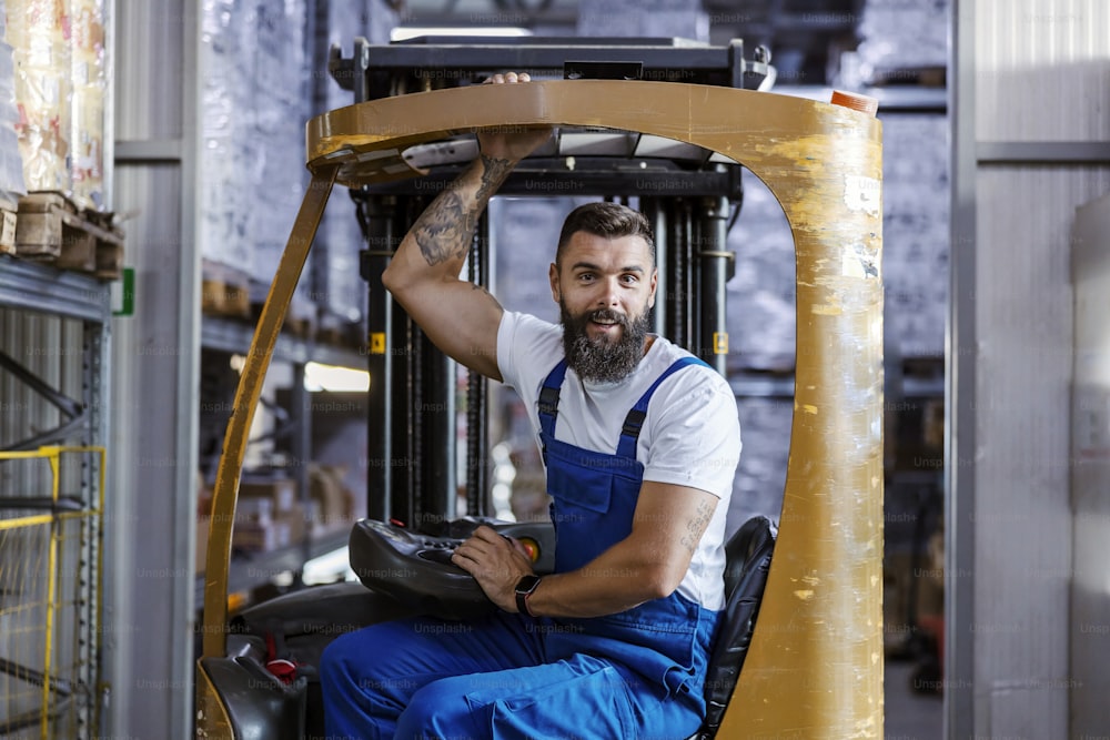 The enthusiastic storage worker is smiling and driving a forklift. Quick reaction and good service is the key of a successful company.