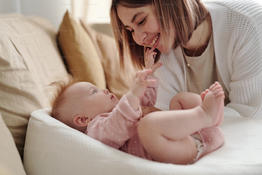 Young smiling woman bending over her cute baby daughter during play after sleep