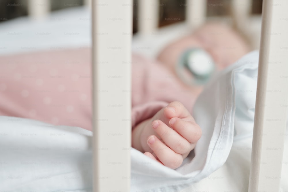 Small fingers and hand of tired baby girl sleeping on white linens in crib