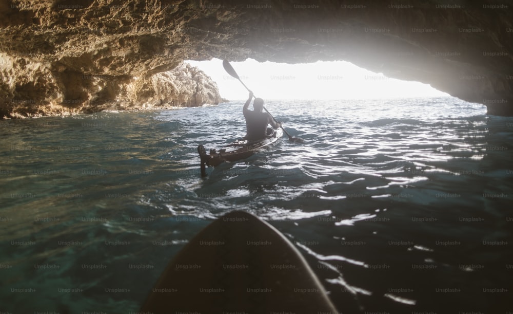 Rückansicht eines Mannes, der in einer Höhle mit dem Kajak paddelt. Kajakfahren und Höhlenforschung zugleich.