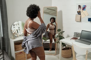 Young attractive female in underwear standing in front of large mirror in bedroom