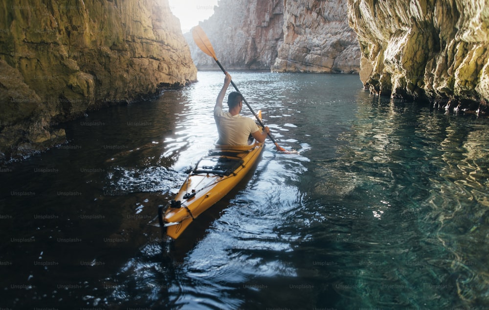 Vista trasera de un hombre remando en kayak en una cueva. Kayak y espeleología al mismo tiempo.