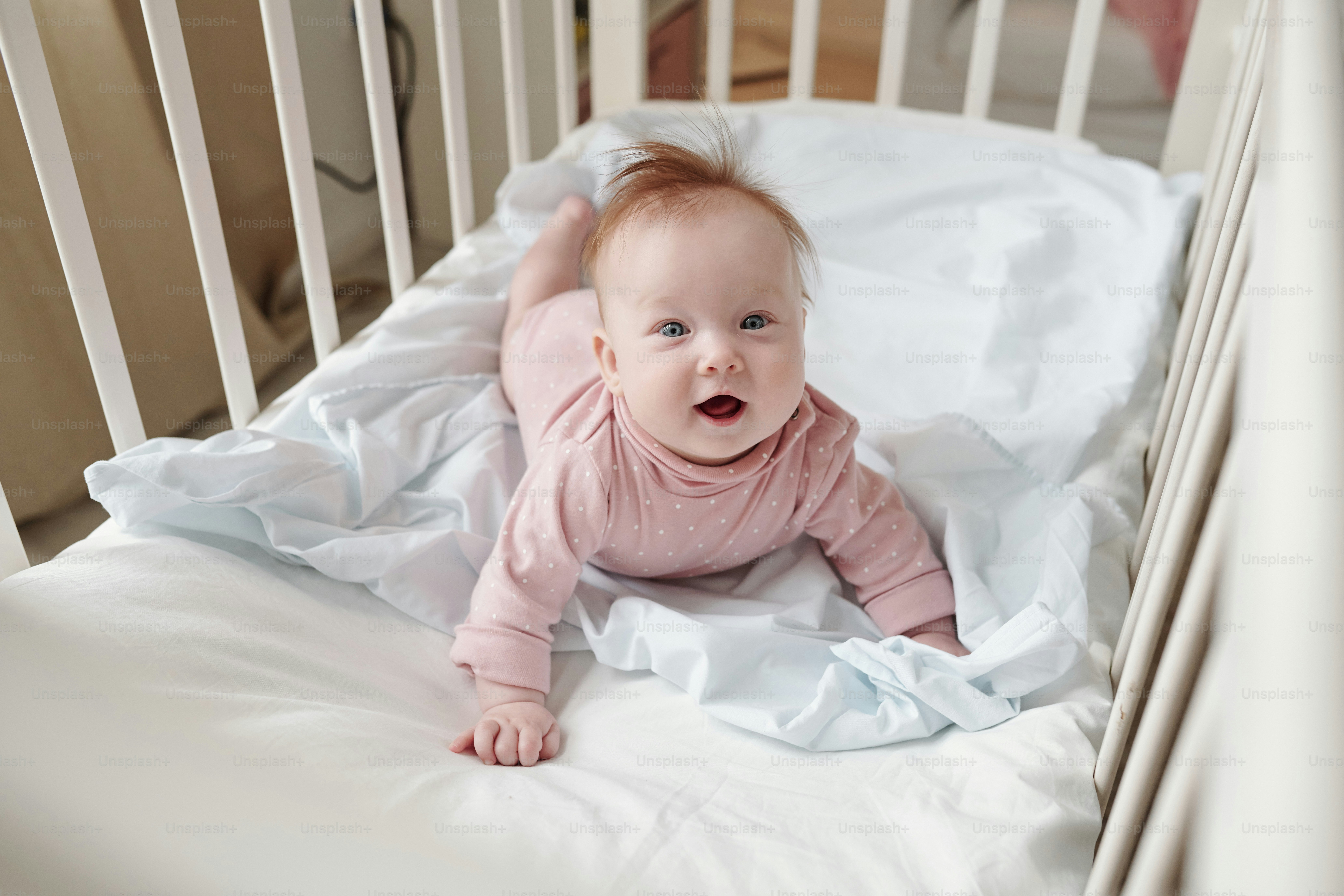 Happy baby girl creeping on white linen in her cradle and looking at camera