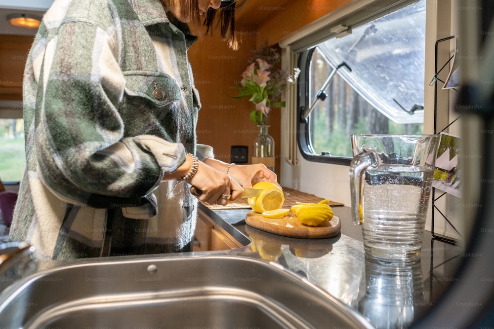 Hände einer jungen Reisenden, die in der Küche des Reisehauses frische Zitrone für Limonade schneiden