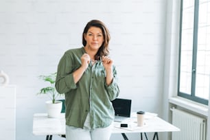 Portrait of Young smiling brunette woman plus size near at laptop on table with house plant in the bright modern office