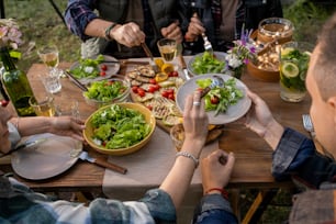 서빙 테이블 옆에서 식사하는 동안 남자 친구의 접시에 야채 샐러드를 놓는 젊은 여성의 손