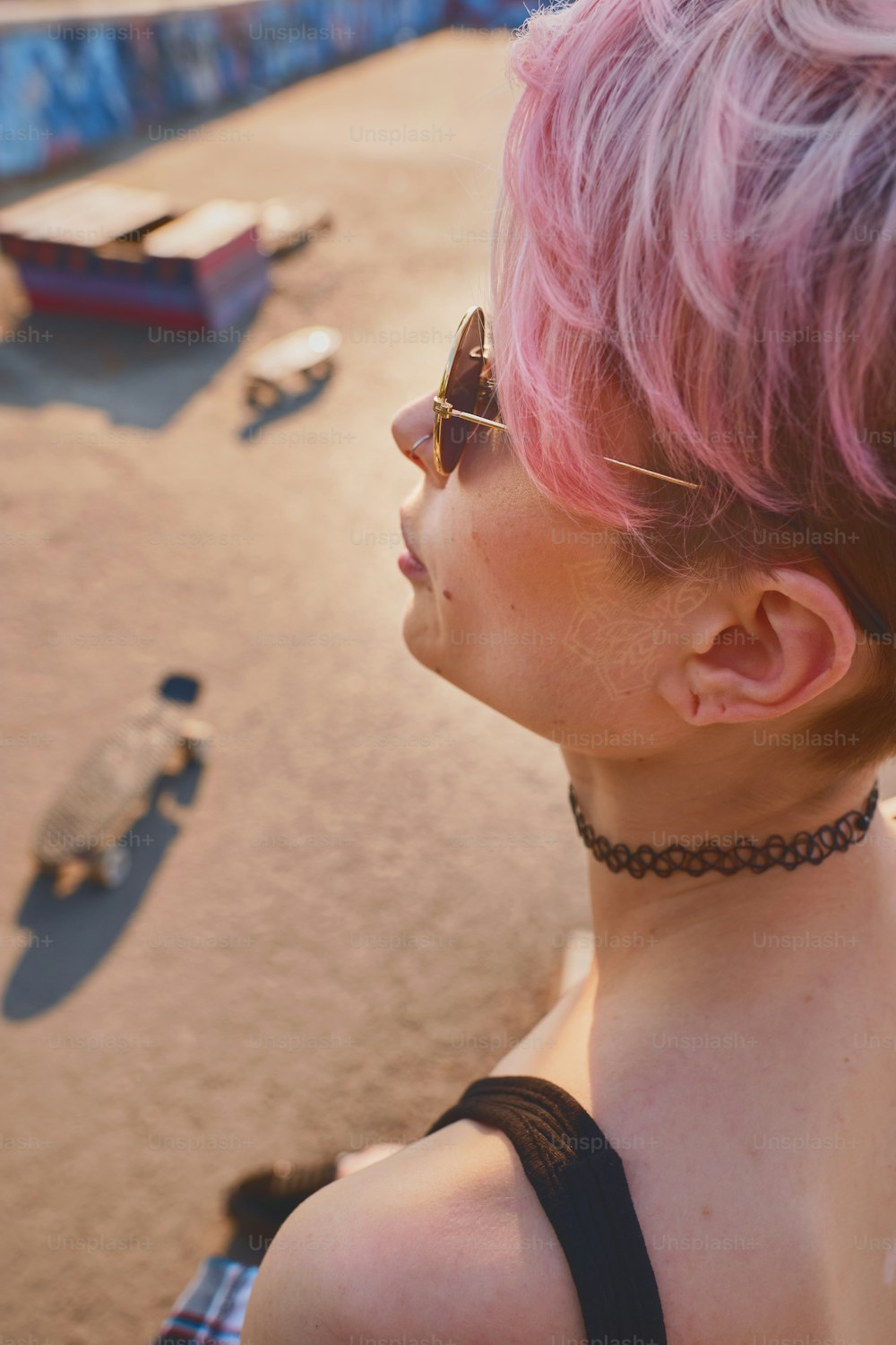 Concept portrait of pink haired female skater outdoors on sunny day with longboard near her