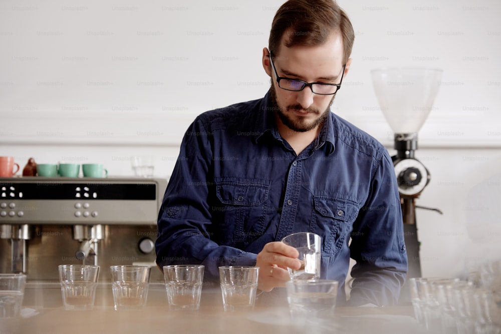 Close up of man's hands tasting freshly brewed coffee in glass cup, using spoon, examining coffee taste and flavour at coffee cupping test for barosta