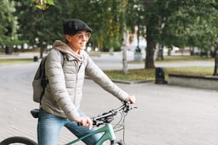 Portrait of fashionable young pretty woman in cap and sunglasses on bicycle on sunny autumn day in city