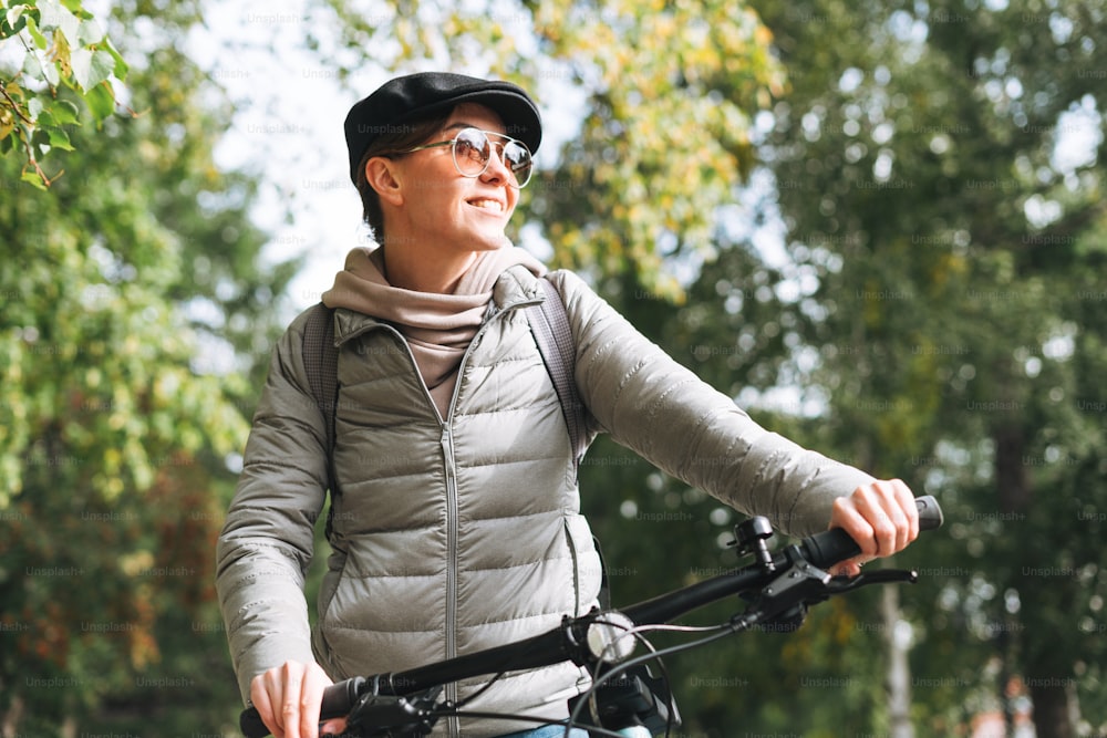 Portrait of fashionable young pretty woman in cap and sunglasses on bicycle on sunny autumn day in city