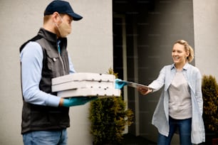 Courier with face mask delivering pizza to female customer during COVID-19 pandemic. Focus is on woman.