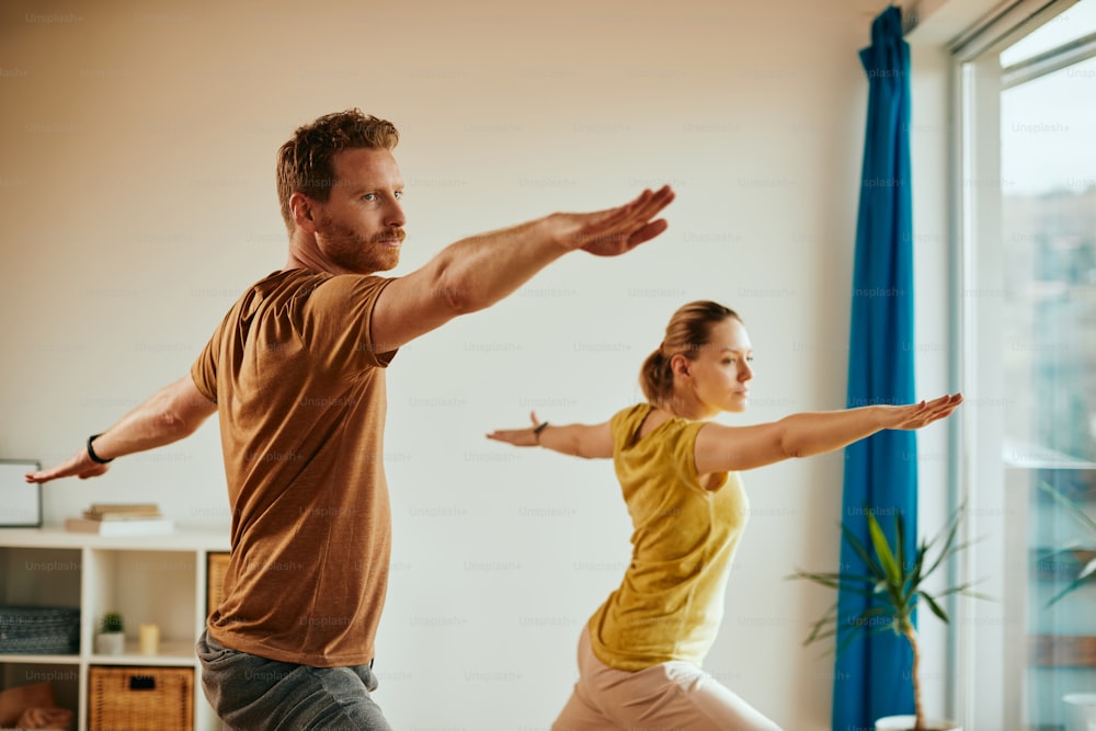 운동 남자와 그의 아내는 집에서 운동하는 동안 요가 스트레칭 운동을 하고 있습니다.