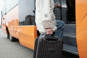 Contemporary senior passenger with suitcase putting leg on staircase while entering bus