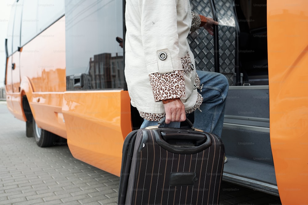 バスに乗り込むときに階段に足を乗せるスーツケースを持つ現代的な年配の乗客