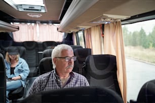 Hombre de edad grave con anteojos sentado junto a la ventana dentro del autobús mientras viaja a otra ciudad