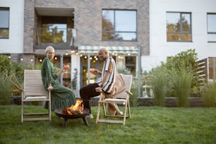 Multiracial couple drinking cocktails during home party in their garden. Burning fire for bbq. Concept of relationship. Modern domestic lifestyle. Black man and european girl enjoying time together