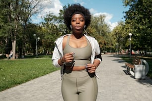 Young plus size sportswoman with earphones jogging in park on sunny morning