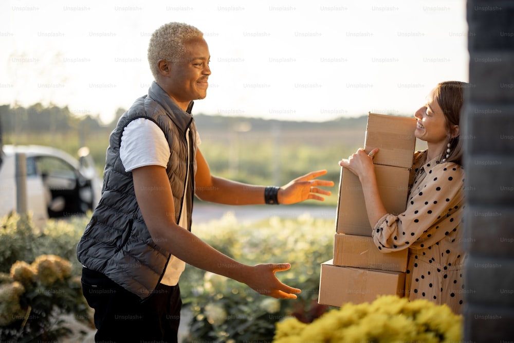 Delivery man giving parcels to caucasian woman on entrance of her house. Young smiling girl taking cardboard boxes. Concept of shipping and logistics. Idea of delivery service
