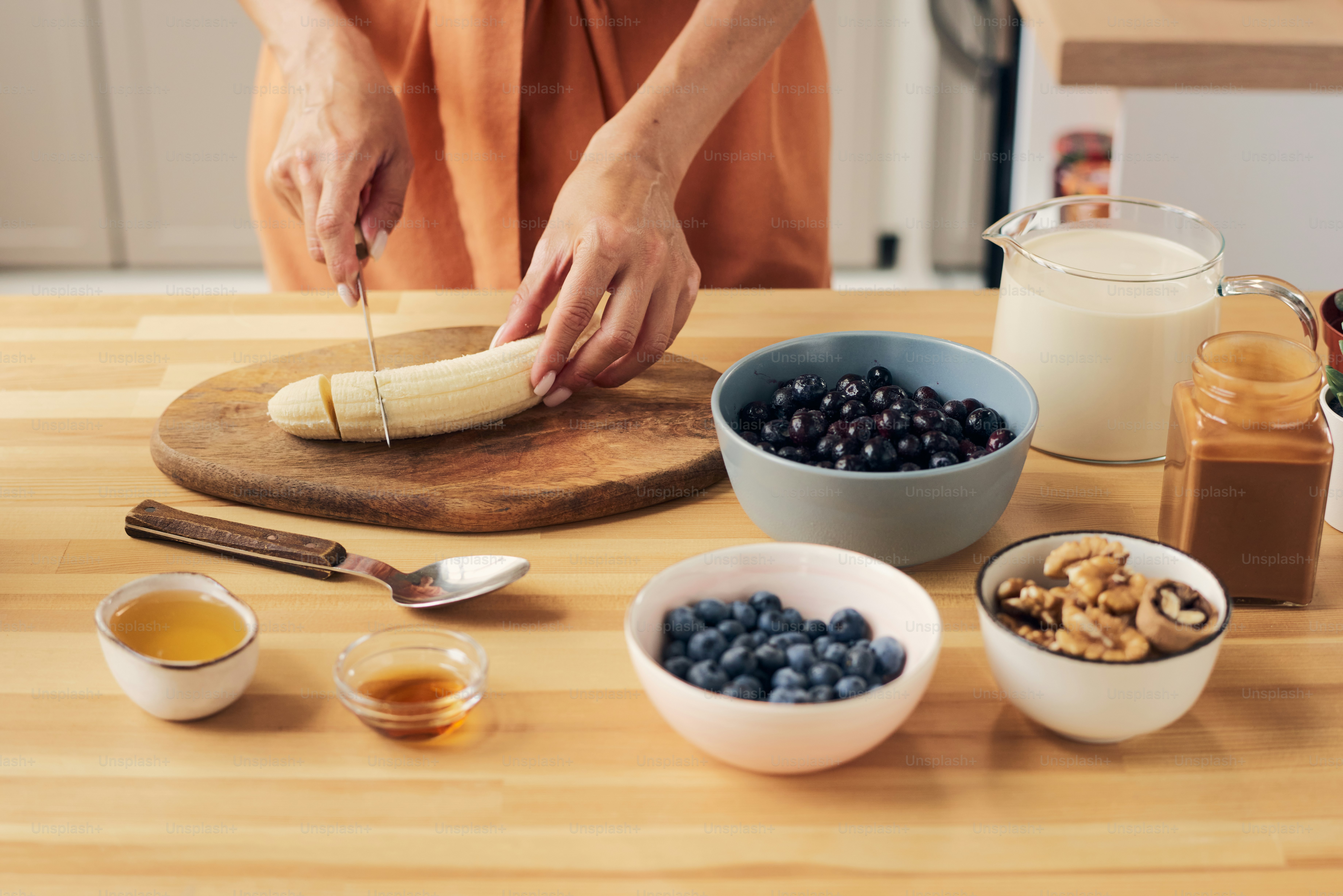 Hände einer jungen Frau, die Bananen auf Holzbrett hackt, für hausgemachten Smoothie