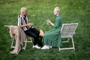 Multiracial couple drinking cocktails during home party on a green lawn in their garden. Burning fire for bbq. Concept of relationship. Black man and european girl enjoying time together